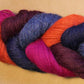 A close-up of a twisted skein of Yarn & Soul's Superfine 400 Alpaca Braid in vibrant colors including magenta, orange, blue, purple, and burgundy, set against a neutral beige background. The sport weight yarn showcases excellent stitch definition.