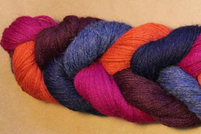 A close-up of a twisted skein of Yarn & Soul's Superfine 400 Alpaca Braid in vibrant colors including magenta, orange, blue, purple, and burgundy, set against a neutral beige background. The sport weight yarn showcases excellent stitch definition.