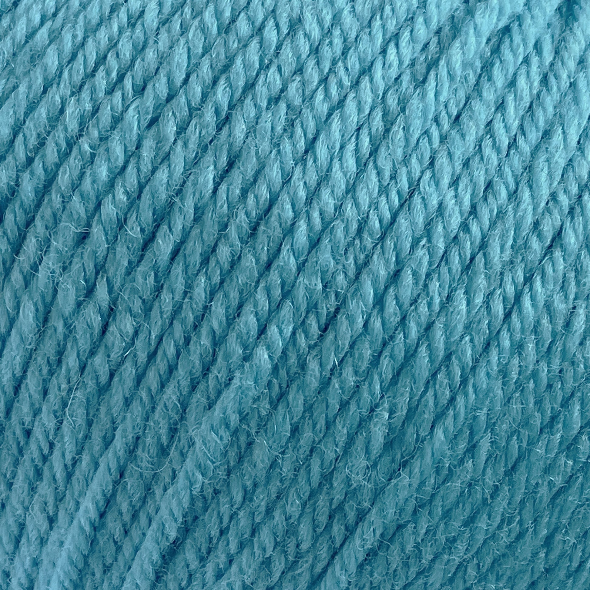 Close-up image of a ball of Cascade 220 Superwash Wool Yarn from Cascade Yarns. The 100% merino wool strands are tightly wound together, showcasing the texture and fibers. The image emphasizes the rich color and beautiful stitch definition of this superwash DK weight yarn.