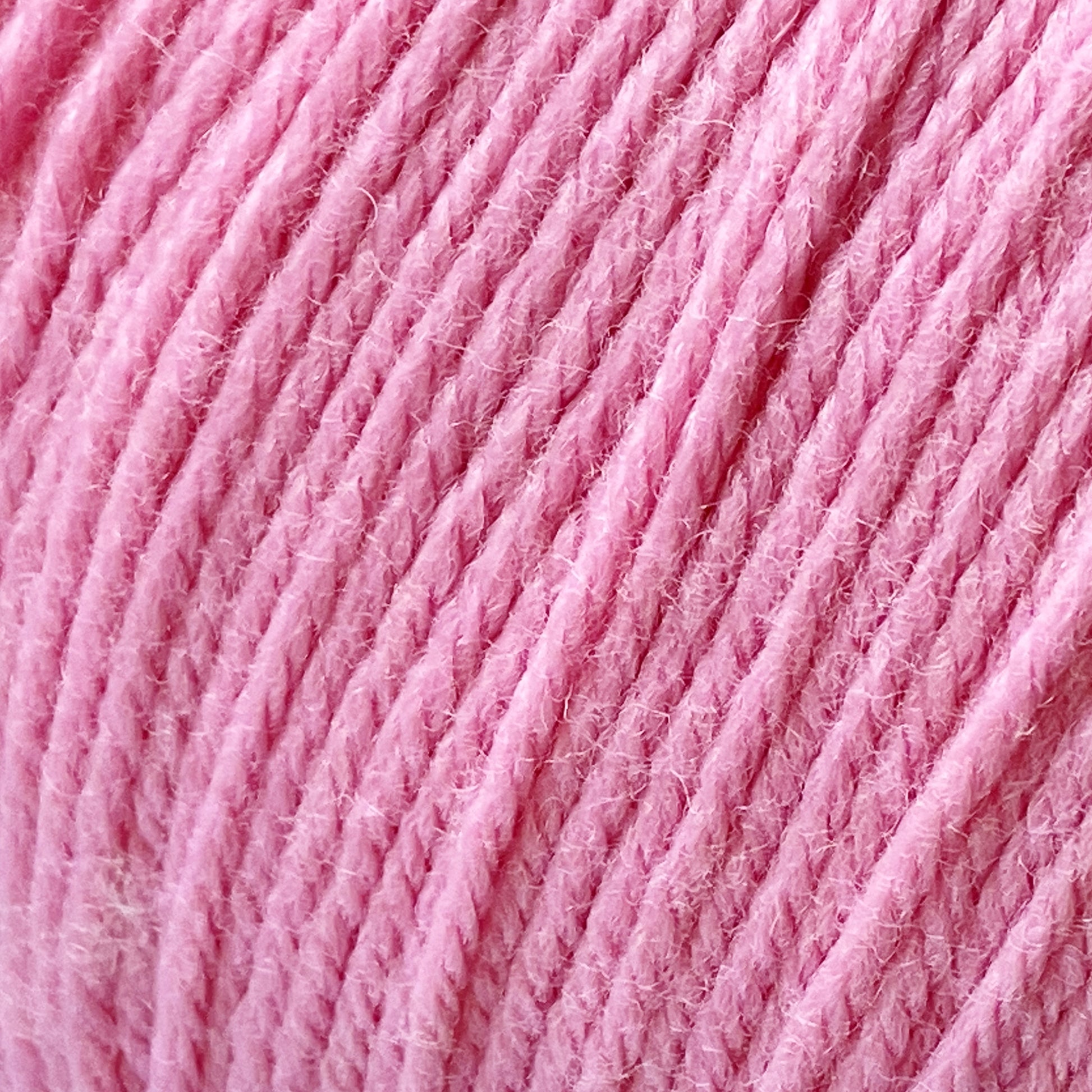 Close-up image of pink Cascade 220 Superwash Wool Yarn. The strands, made from 100% merino wool by Cascade Yarns, are neatly wound and tightly coiled, giving the appearance of a soft texture with slight fuzziness. The image highlights the intricate detailing, fine twists of the fibers, and beautiful stitch definition.