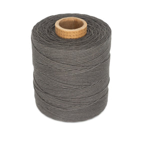 A spool of Stuart C. Hurlbert & Co.'s #9 Cotton Lacing Cord is wrapped around a cylindrical core with a wooden opening. The dark gray thread appears thick and tightly wound, suitable for sewing or crafting purposes like braided rugs or as a cotton rug lacing cord. The background is plain white.