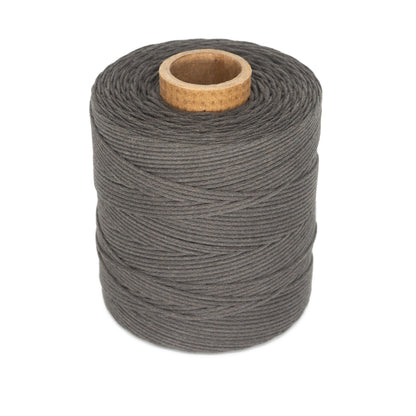 A spool of Stuart C. Hurlbert & Co.'s #9 Cotton Lacing Cord is wrapped around a cylindrical core with a wooden opening. The dark gray thread appears thick and tightly wound, suitable for crafting purposes like braided rugs or as a cotton rug lacing cord. The background is plain white.