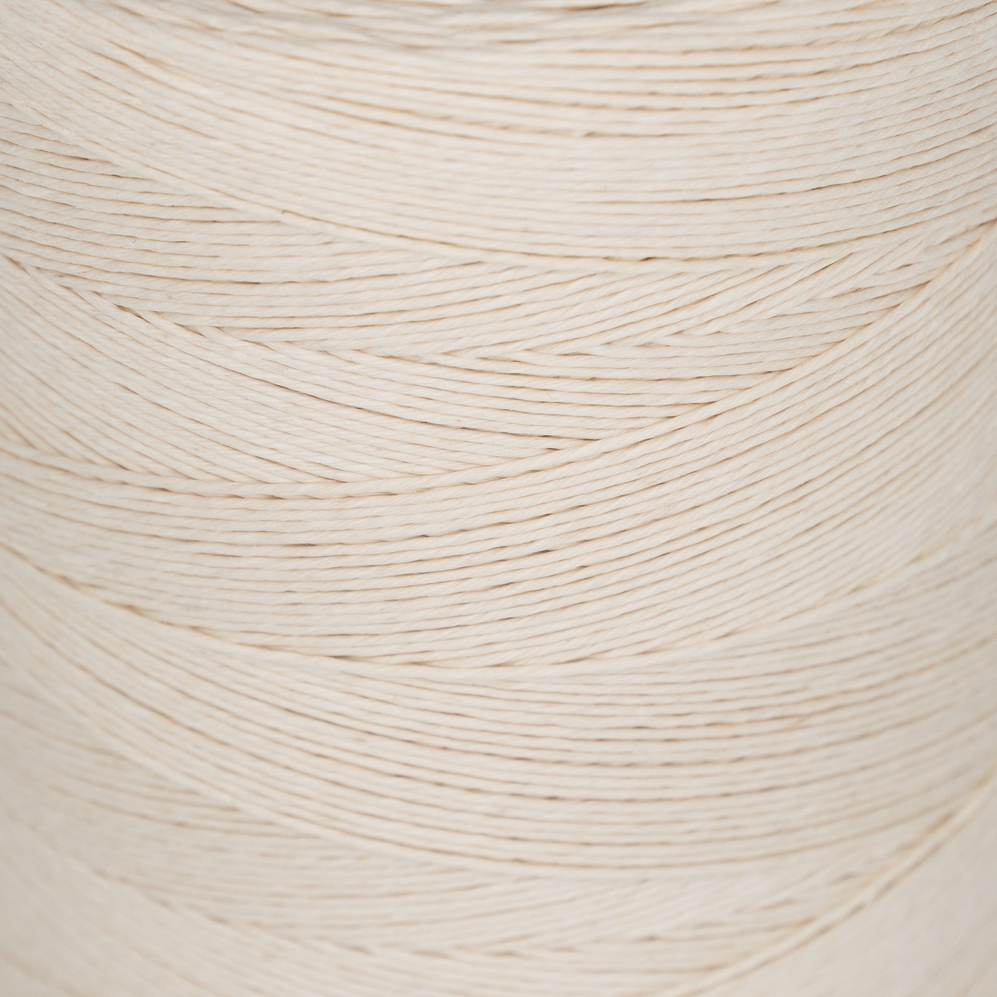 Close-up image of tightly wound 20/6 Linen Rug Lacing (Natural White) from Stuart C. Hurlbert & Co. on a spool, showcasing the texture and alignment of the individual strands in a diagonal, overlapping pattern. Ideal for braided rugs or rug warp projects.