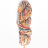 A skein of Universal Yarns' Bamboo Bloom Handpaints multi-colored yarn features a mix of warm hues, including red, orange, yellow, grey, and beige. This tightly coiled yarn showcases its soft, fuzzy texture against a plain white background.