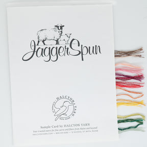 The JaggerSpun Sample Card from Jagger Brothers, Inc. features an illustration of a sheep and includes yarn samples in diverse colors and styles: dark brown, light brown, green, red, light pink, yellow, orange, and white. This makes it a versatile design resource.