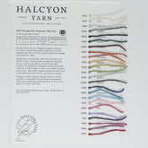 The Patagonia Organic Merino Juniper Moon Farm Sample Card from Halcyon Yarn includes 18 labeled strands of 100% Patagonia Organic Merino wool in a spectrum of colors such as white, greys, green, yellow, red, blue, and purple. The card provides detailed specifications of the wool along with contact information for both Halcyon Yarn and Juniper Moon Farm.