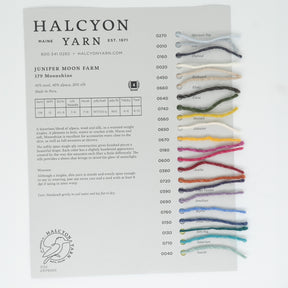 The Moonshine Sample Card from Halcyon Yarn highlights Juniper Moon Farm's luxurious Moonshine Yarn samples, featuring a variety of colors labeled with their respective names and item numbers. The card provides detailed information on the yarn's premium blend composition and suggested uses, with the Halcyon Yarn logo displayed at the bottom.