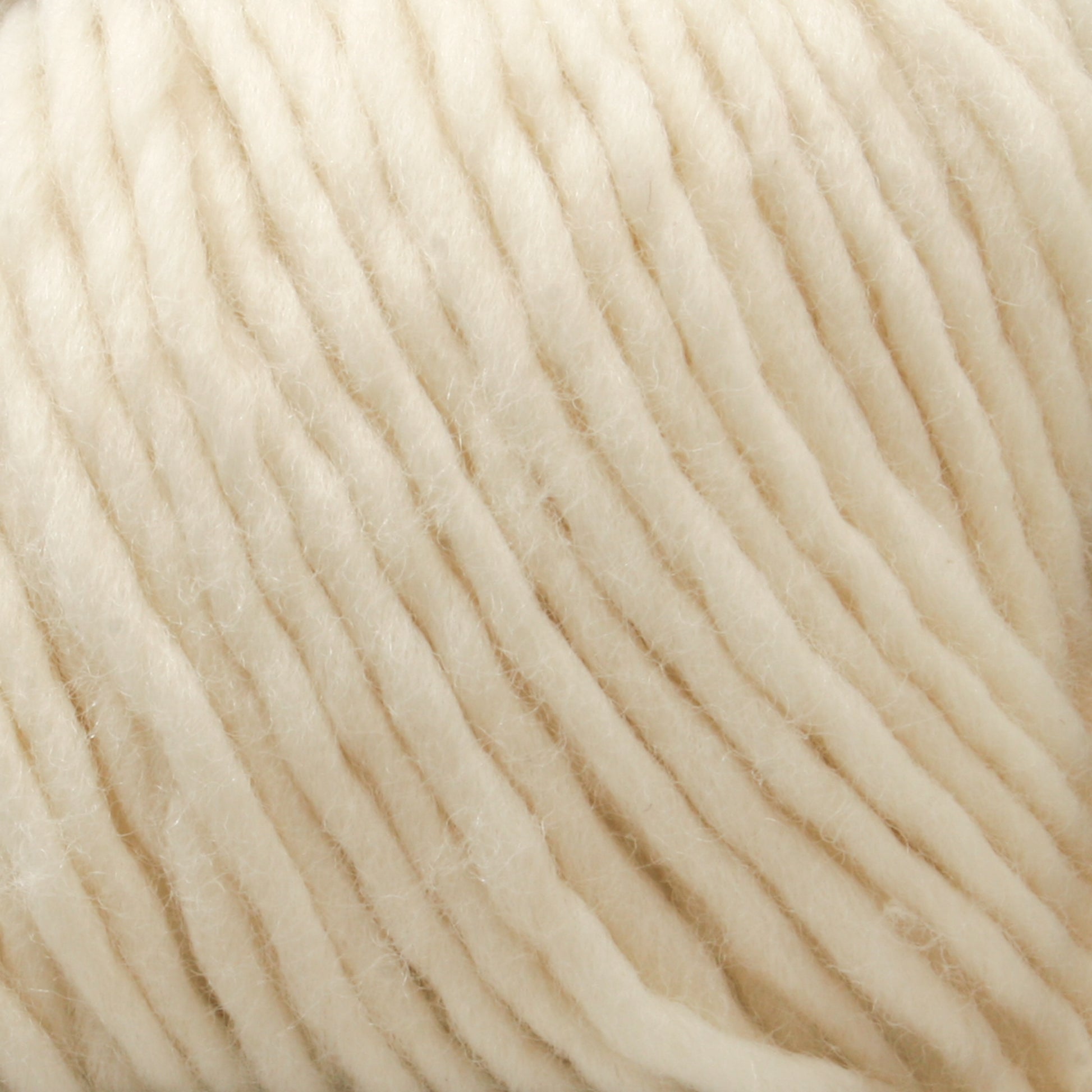 Close-up of a ball of thick, cream-colored Malabrigo Merino Worsted Wool Yarn from Malabrigo Yarn. The yarn has a soft and fluffy texture, with individual strands tightly spun together, creating a slightly rippled, linear pattern. This cozy and inviting worsted weight gauge yarn is perfect for knitting or crocheting.