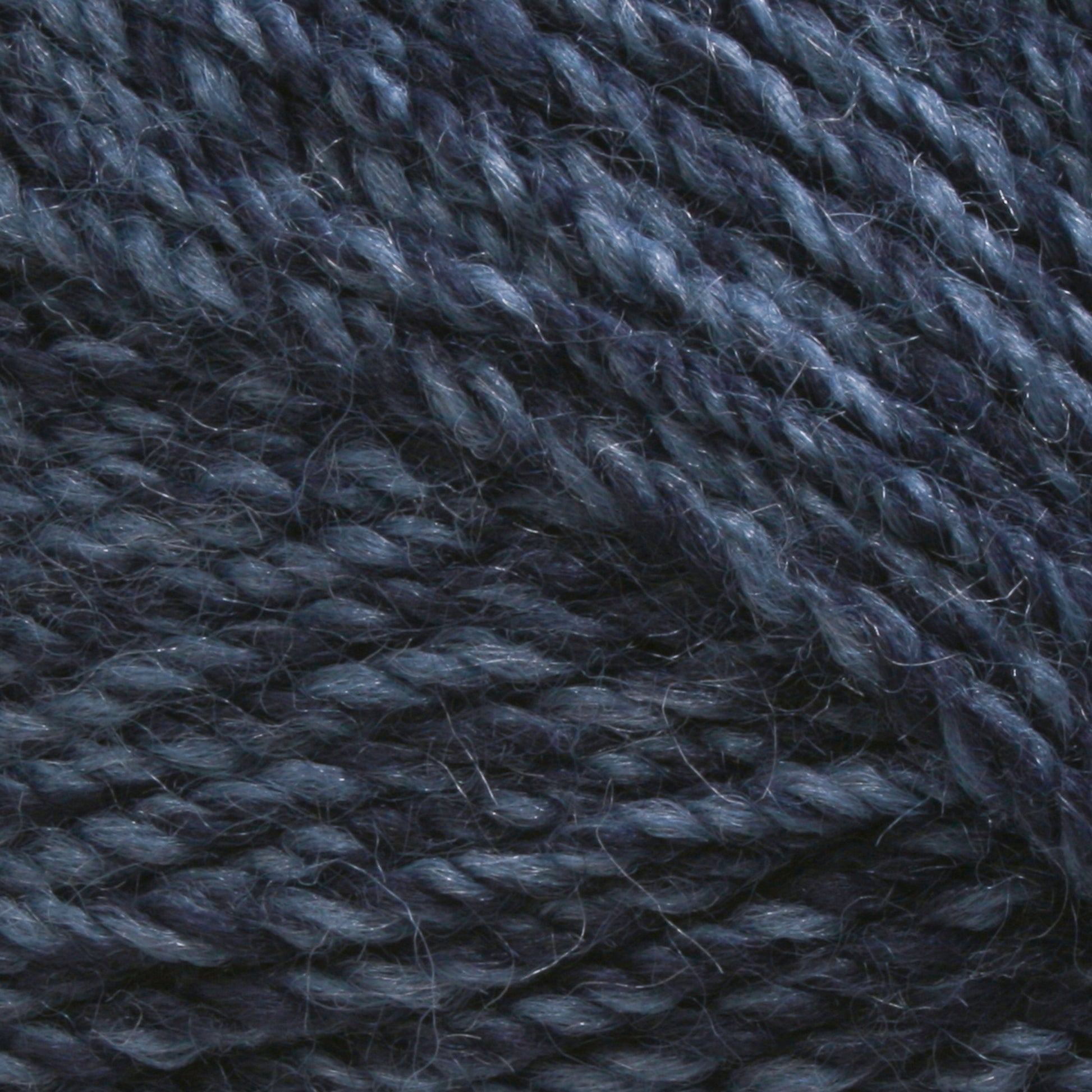 Close-up of Plymouth Encore Worsted Yarn by Plymouth Yarn Co. in a dark blue shade, showcasing its slightly shiny and textured appearance. The strands are tightly twisted together, accentuating the individual fibers and offering a rich, detailed texture. This economical yarn is also machine washable, making it an ideal choice for various projects.