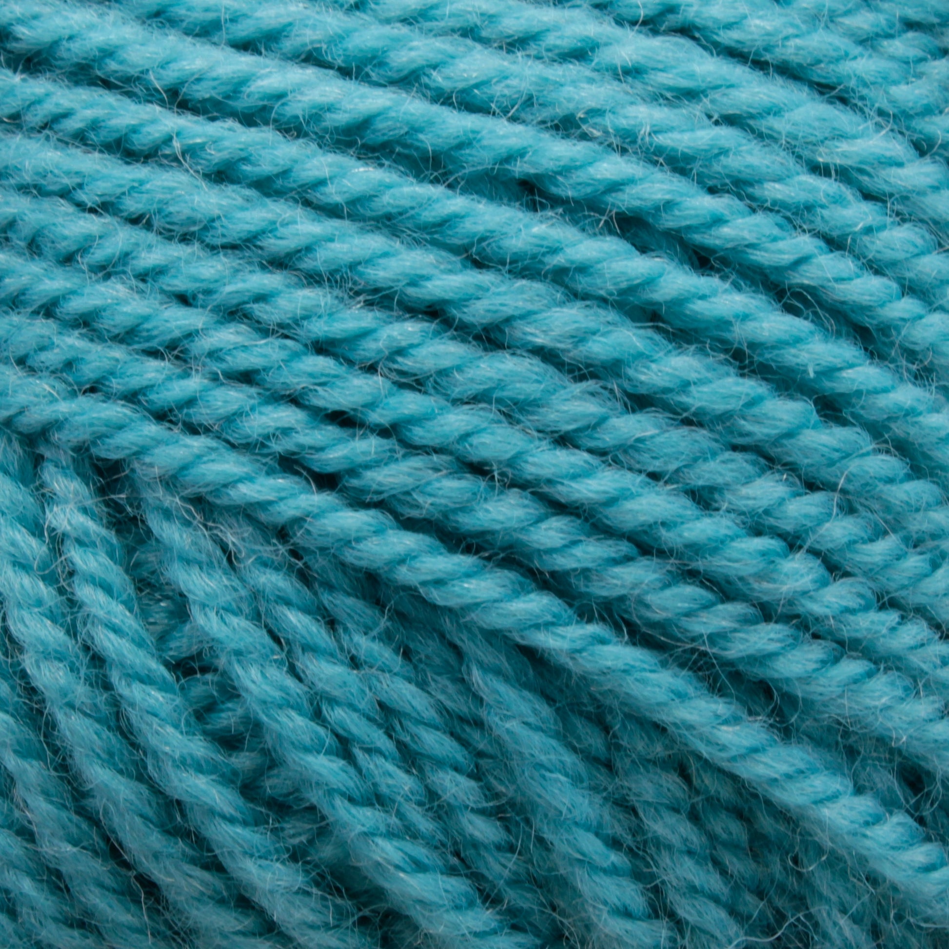 Close-up image of Plymouth Encore Worsted Yarn by Plymouth Yarn Co. in turquoise blue. The texture shows tightly wound strands with a slightly fuzzy surface, emphasizing the soft and fibrous nature of the machine washable yarn. The color appears even and vibrant throughout the image, making it an economical option for various projects.