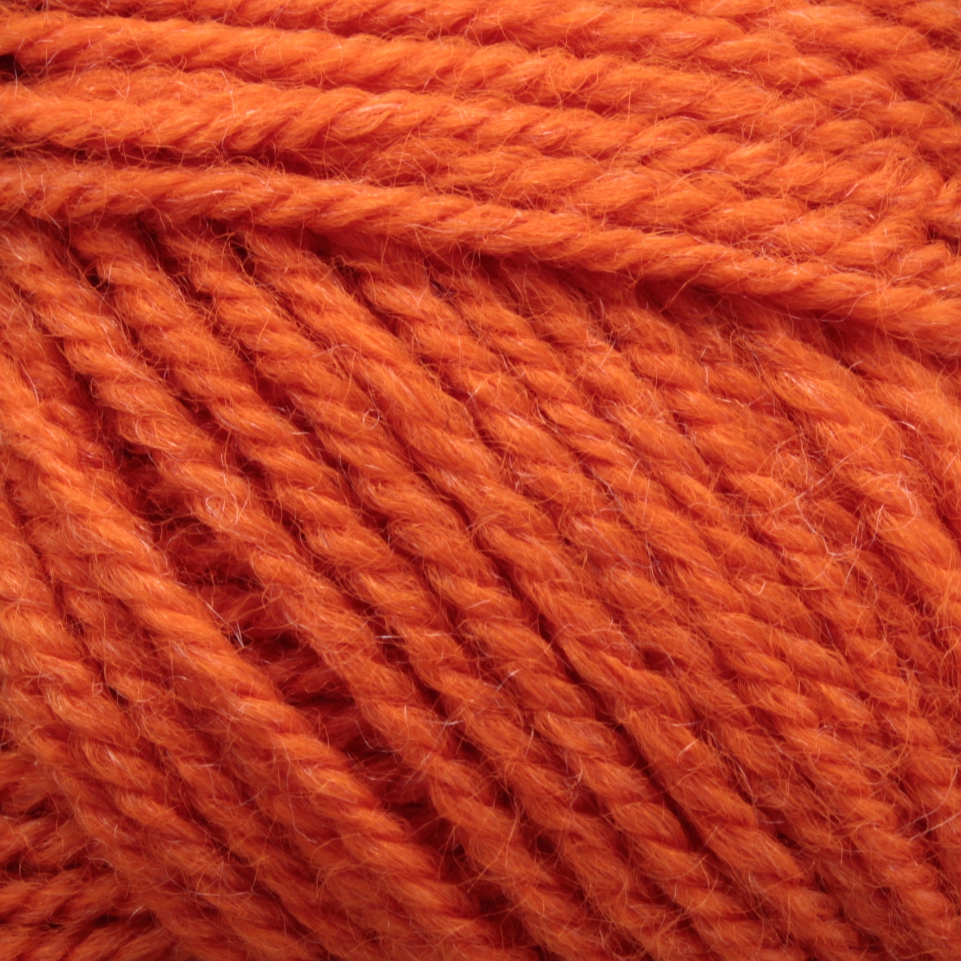 Close-up image of bright orange Plymouth Encore Worsted Yarn by Plymouth Yarn Co. The texture of this high-quality, economical option is visible, showcasing tightly twisted strands that are also machine washable.