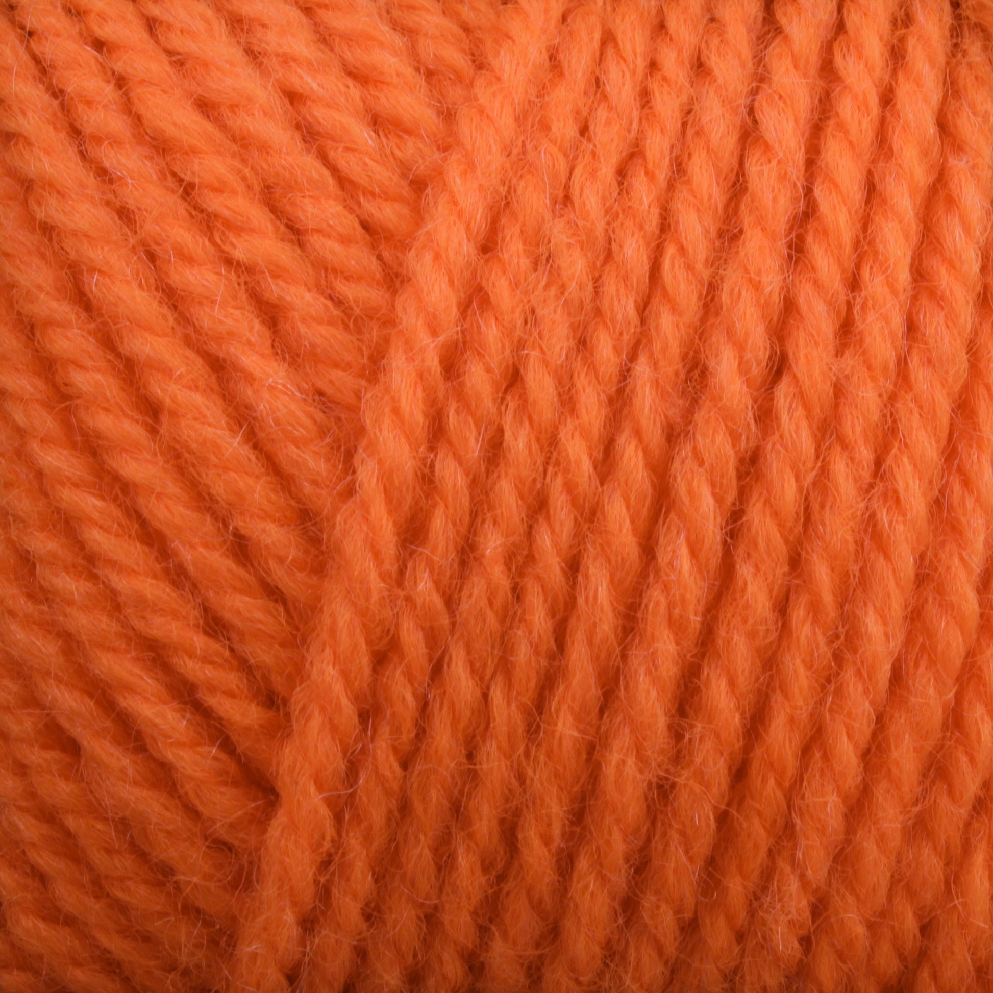 Close-up image of thick, orange Plymouth Encore Worsted Yarn by Plymouth Yarn Co., showcasing the tightly twisted fibers and detailed texture. The yarn appears soft and fluffy with a warm, vibrant hue, perfect for knitting or crocheting various crafts. This machine washable yarn provides an economical option for your creative projects.