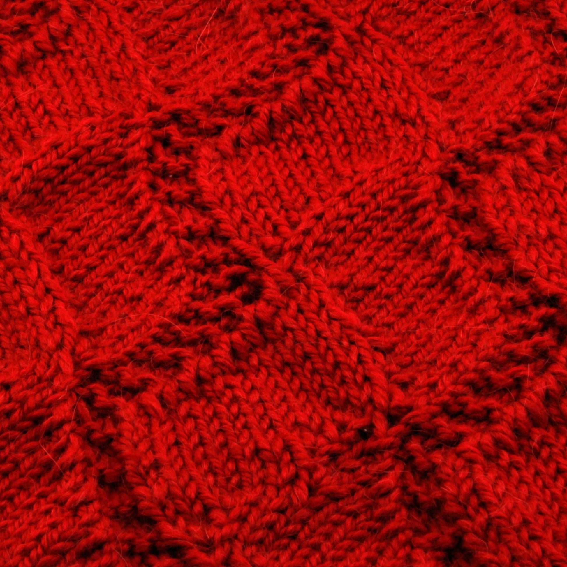 Close-up of the Peruby Waves Throw by Halcyon Yarn showcasing a textured diamond pattern. The knitting features intricate stitches with varying depths, creating a rich, tactile surface. The warm, vibrant red color and chunky yarn dominate the image, highlighting its handmade beauty.