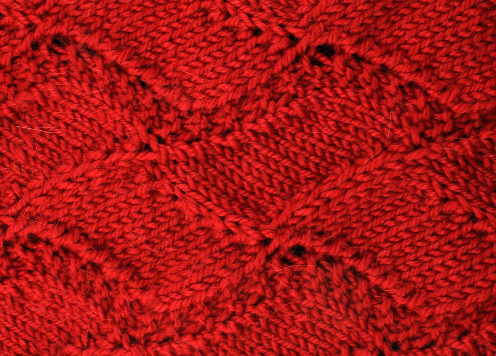 A close-up of the Peruby Waves Throw from Halcyon Yarn, showcasing its red knitted fabric with a textured, interlocking diamond pattern. The uniform stitches highlight the intricate wave stitch pattern and craftsmanship. The material appears warm and cozy, ideal for winter garments like sweaters or blankets made with chunky yarn.