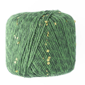 A close-up of Jo Sharp Lumina, a green DK weight yarn from Kingfisher Yarn & Fibre, adorned with small gold sequins. The yarn is tightly wound and has a textured appearance, with the sequins adding a subtle sparkle. Knitting needles rest in the background, which is plain and white, drawing attention to the intricate details of Jo Sharp Lumina.