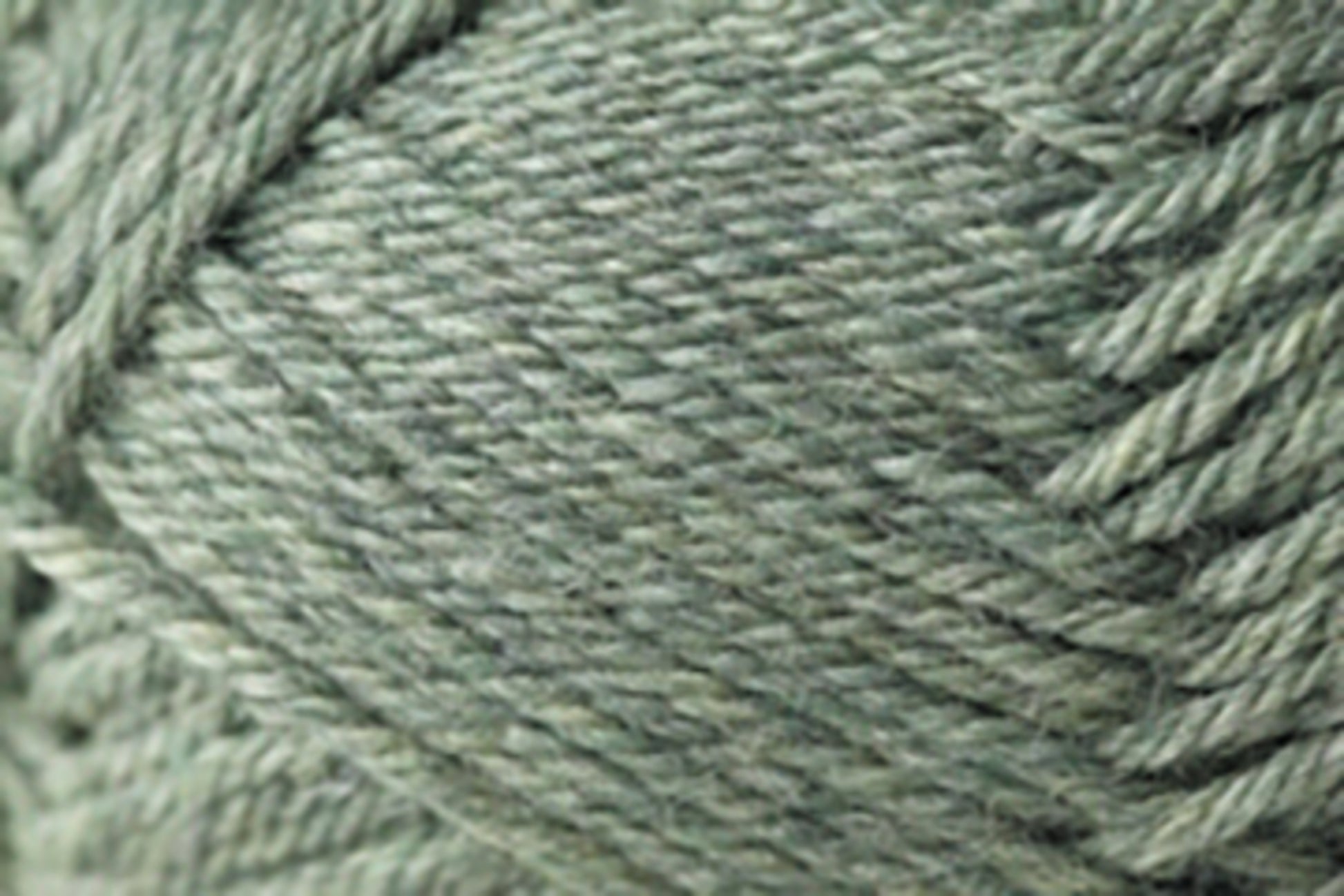 Close-up view of a ball of Jo Sharp Classic DK Wool yarn from Kingfisher Yarn & Fibre, featuring tightly wrapped strands with a slight sheen. The soft, green texture and weaving pattern are visible, highlighting the intricate details of this versatile DK gauge yarn. Ideal for knitting, crocheting, or crafting projects.