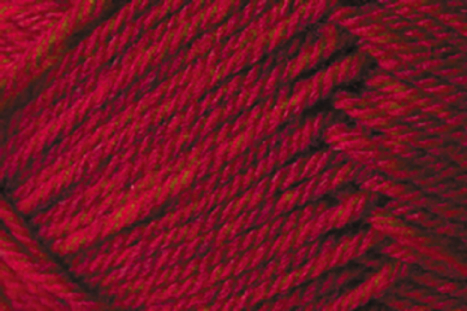 Close-up image of red yarn with visible fibers and strands twisted together, showing a textured pattern. The yarn appears soft and tightly spun, ideal for knitting or crocheting projects. This Jo Sharp Classic DK Wool by Kingfisher Yarn & Fibre showcases a vibrant red with subtle variations in shade, perfect for versatile DK gauge creations.