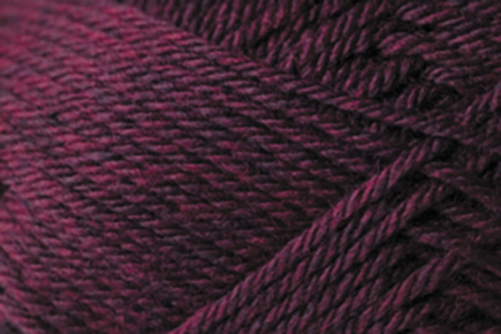 Close-up image of dark maroon Jo Sharp Classic DK Wool fibers from Kingfisher Yarn & Fibre, wound together in a neat, textured pattern. The strands of this versatile yarn appear soft and dense, with slight variations in color intensity throughout the premium-grade wool.