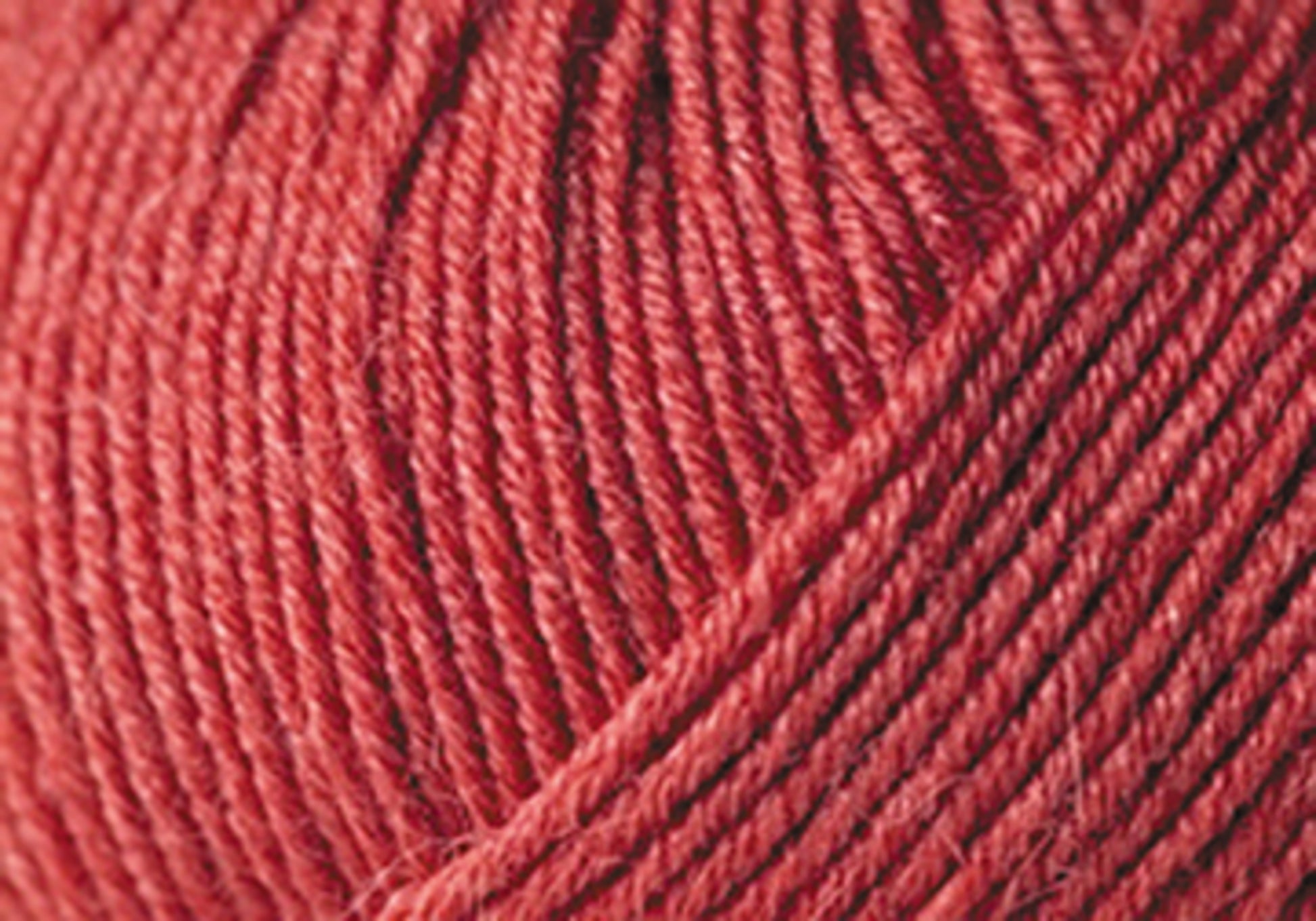 Close-up of a ball of Jo Sharp Mulberry Silk Georgette Yarn by Kingfisher Yarn & Fibre. The texture is detailed and the yarn is tightly wound, showcasing the fine fibers and consistent weave. The color appears to be rich and vibrant, with slight variations in the shade—perfect for crafting heirloom items.