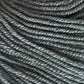 Close-up view of dark gray yarn, showing the texture and twisted strands. The yarn, made from Jo Sharp Mulberry Silk Georgette Yarn by Kingfisher Yarn & Fibre, appears in a dense pattern with even, tight coils, highlighting the fibrous material.