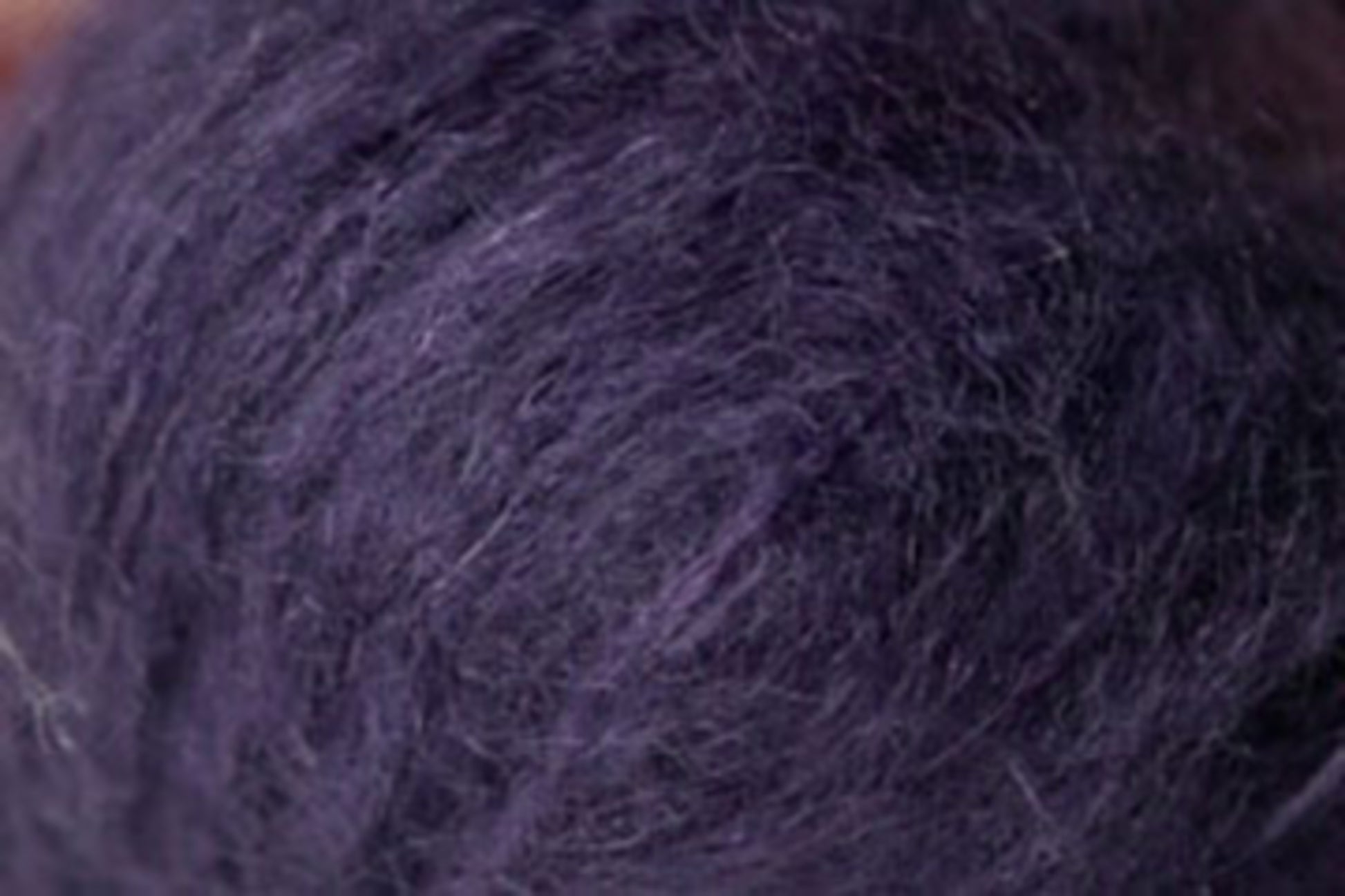 Close-up image of a ball of thick, fuzzy, dark purple yarn. The texture is soft and slightly fluffy, showcasing the Jo Sharp Rare Comfort Kid Mohair fibers and strands intertwined together, crafted by Kingfisher Yarn & Fibre.