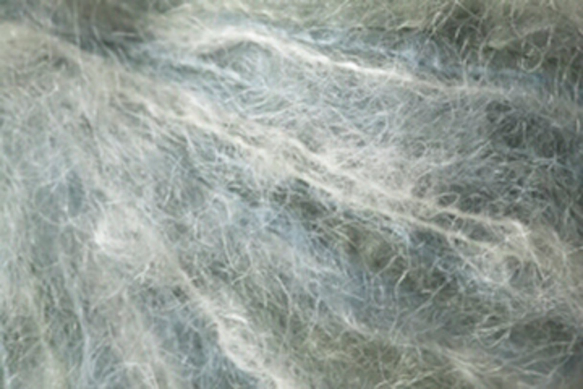 Close-up of light and wispy, semi-transparent fibers intertwined in an abstract pattern. The fibers have a soft, airy appearance, with shades of white and pale blue blending together, akin to Kingfisher Yarn & Fibre's Jo Sharp Rare Comfort Kid Mohair yarns, creating a delicate, ethereal texture.