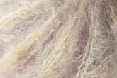 Close-up image showcasing the light-colored, fluffy, and woolly texture of Jo Sharp Rare Comfort Kid Mohair from Kingfisher Yarn & Fibre. The fibers are soft and display a mix of pale beige and faint purple hues, interwoven to create a fuzzy, delicate surface that's perfect for luxurious comfort in airy sweaters.