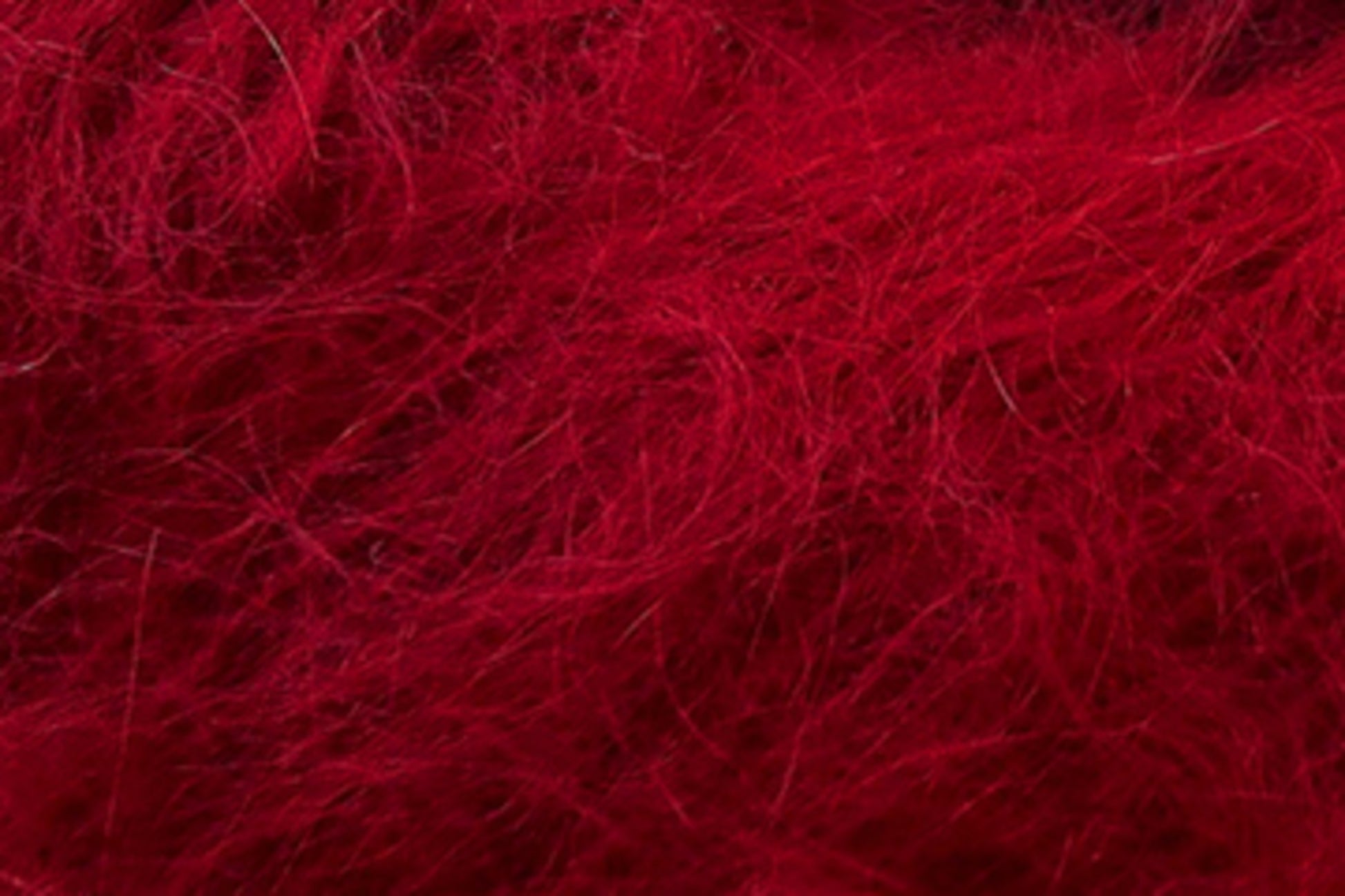 A close-up image of Jo Sharp Rare Comfort Kid Mohair by Kingfisher Yarn & Fibre, showcasing its red fibrous material with a tangled and fuzzy texture. The fibers appear soft and wispy, creating a dense and intricate pattern across the image, resembling wool or synthetic fur.