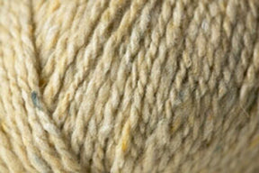 Close-up of a ball of luxurious yarn with rich tweed highlights, featuring slight variations in color and texture. Showcasing the soft, twisted fibers and natural appearance, the Kingfisher Yarn & Fibre's Jo Sharp Silkroad Aran Tweed appears thick and perfect for knitting or crocheting warm, cozy items.