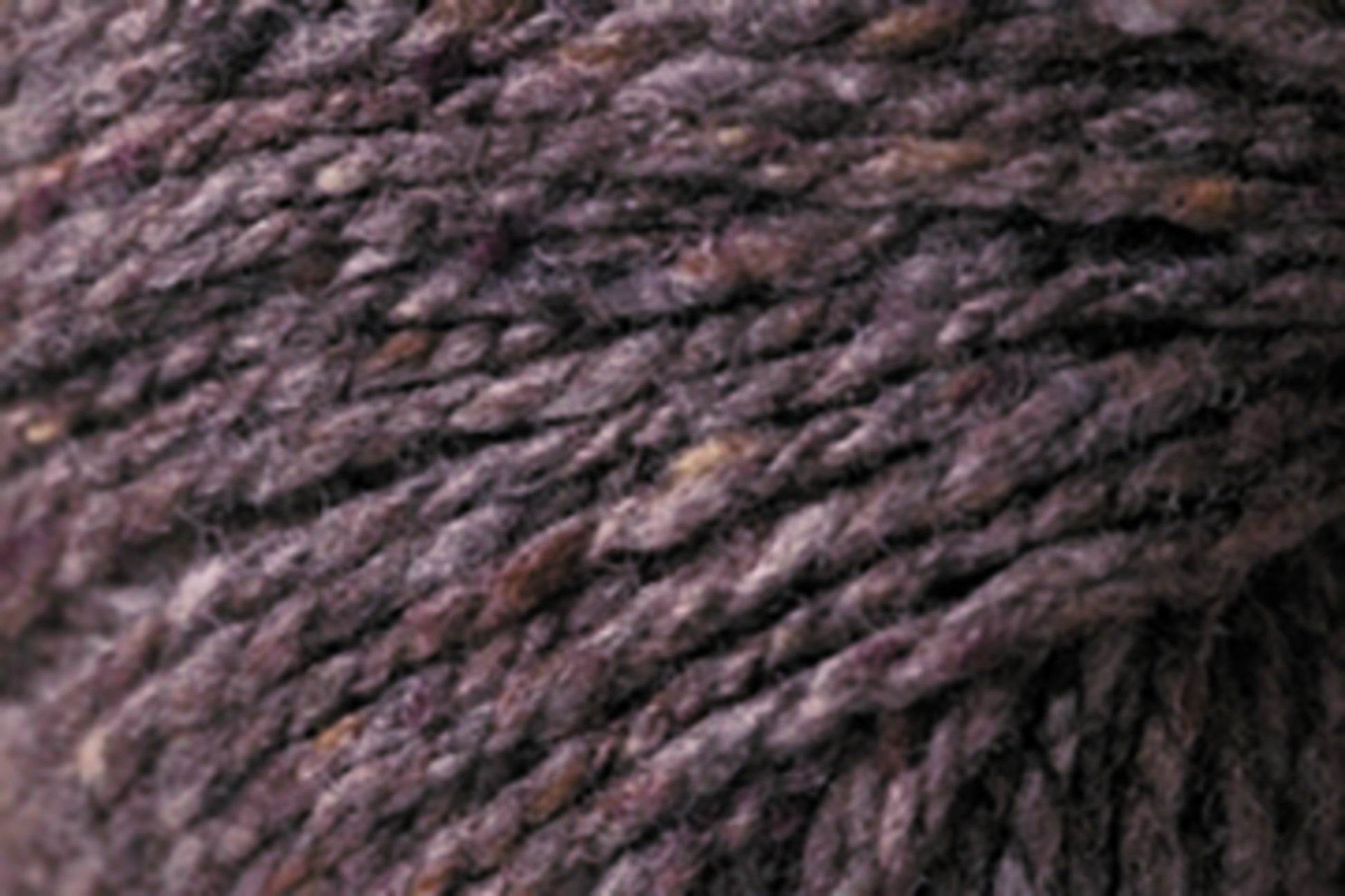 Close-up of a textured ball of Kingfisher Yarn & Fibre's Jo Sharp Silkroad Aran Tweed in varying shades of purple and grey. The strands are tightly spun, showcasing the natural fibers and slight color variations. Rich tweed highlights emphasize the intricate details and softness of this luxurious yarn.