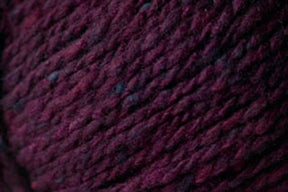 Close-up image of thick, dark burgundy Kingfisher Yarn & Fibre's Jo Sharp Silkroad Aran Tweed with subtle variations in color, displaying a textured, woven appearance. The yarn's fibers are slightly mottled, indicating a rich and soft texture that is suitable for knitting or crocheting.