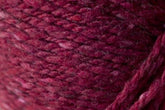 Close-up image of luxurious, burgundy-colored yarn with a slightly textured, woven appearance. The Kingfisher Yarn & Fibre's Jo Sharp Silkroad Aran Tweed fibers showcase varying shades of red with subtle flecks of lighter and darker hues, resulting in rich tweed highlights and a tactile quality.