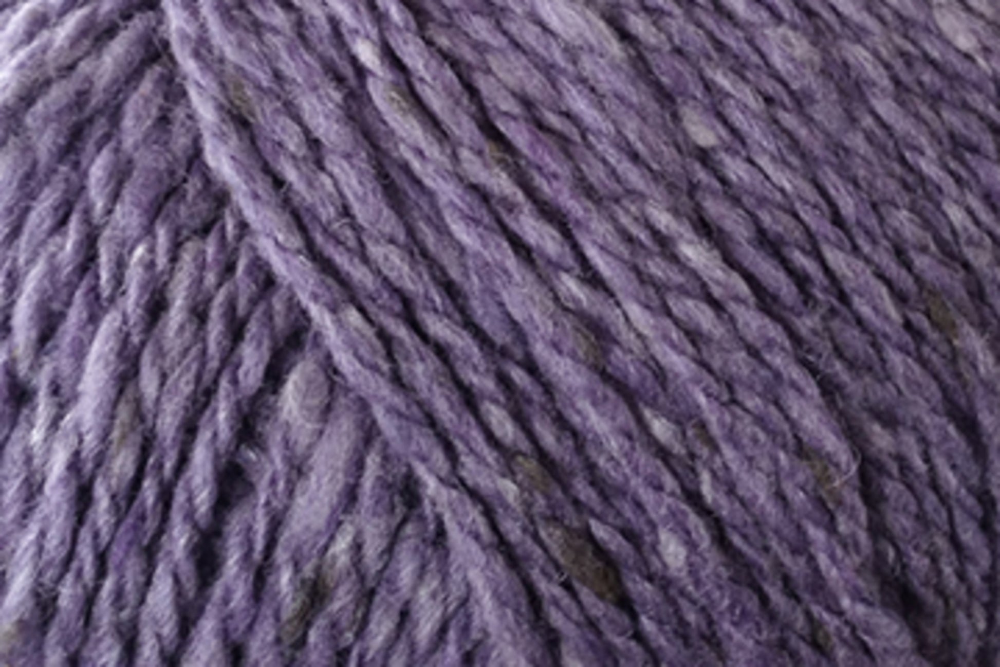 Close-up of Jo Sharp Silkroad Aran Tweed yarn by Kingfisher Yarn & Fibre, showcasing its thick, purple strands with a slightly textured appearance. The intertwined fibers appear soft and cozy, evoking a wool-like texture. This luxurious yarn features subtle variations in color and rich tweed highlights, adding depth to its overall look.