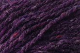 Close-up image of luxurious purple yarn with rich tweed highlights and hints of red, showcasing its texture and fibers. The Kingfisher Yarn & Fibre Jo Sharp Silkroad Aran Tweed appears thick and slightly fuzzy, with visible strands twisted together.