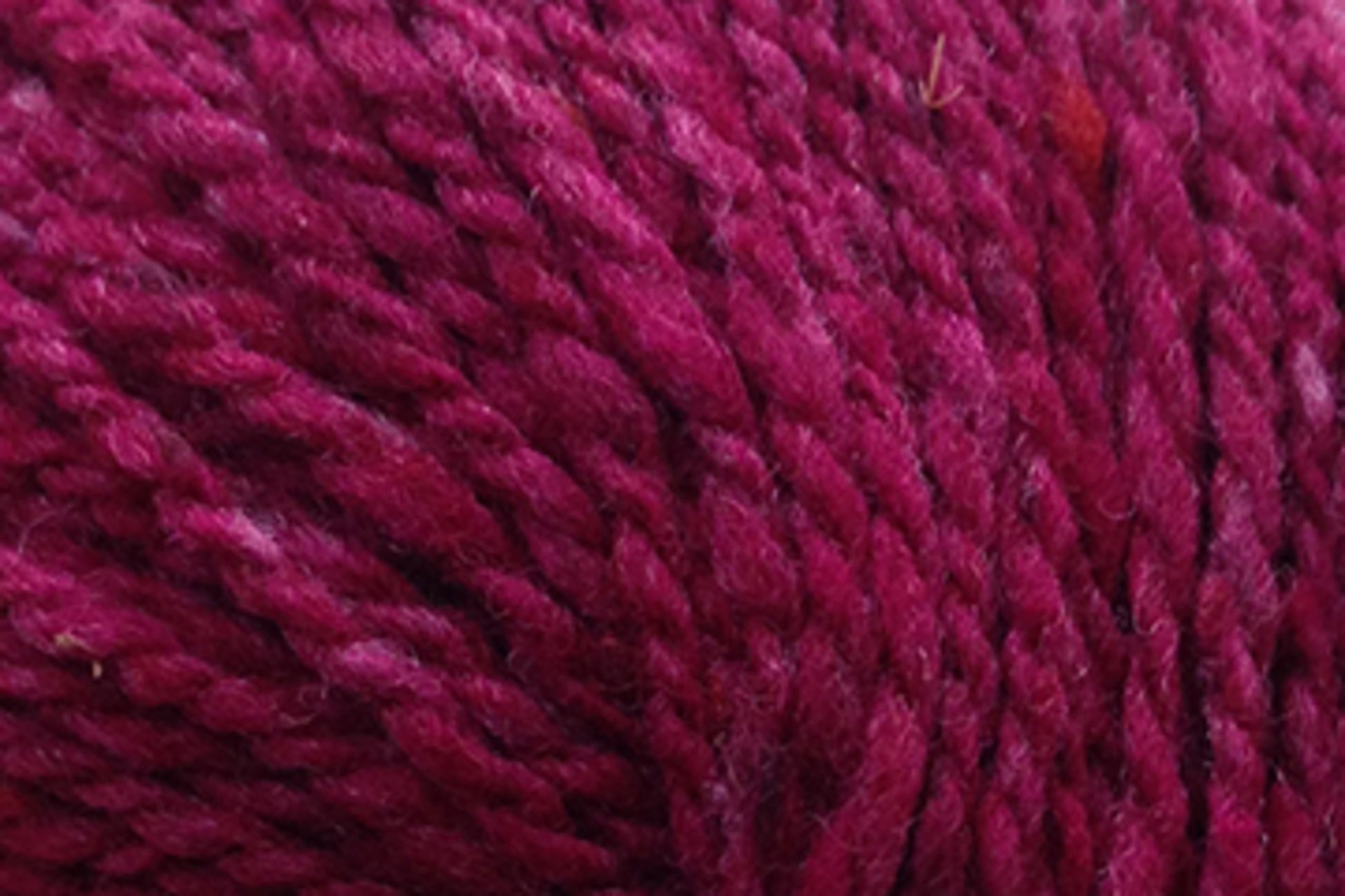 Close-up image of deep magenta-colored Kingfisher Yarn & Fibre Jo Sharp Silkroad Aran Tweed yarn, showing the texture and individual threads twisted together. The surface appears soft and woolly with rich tweed highlights, making it a luxurious yarn suitable for knitting or crocheting projects.