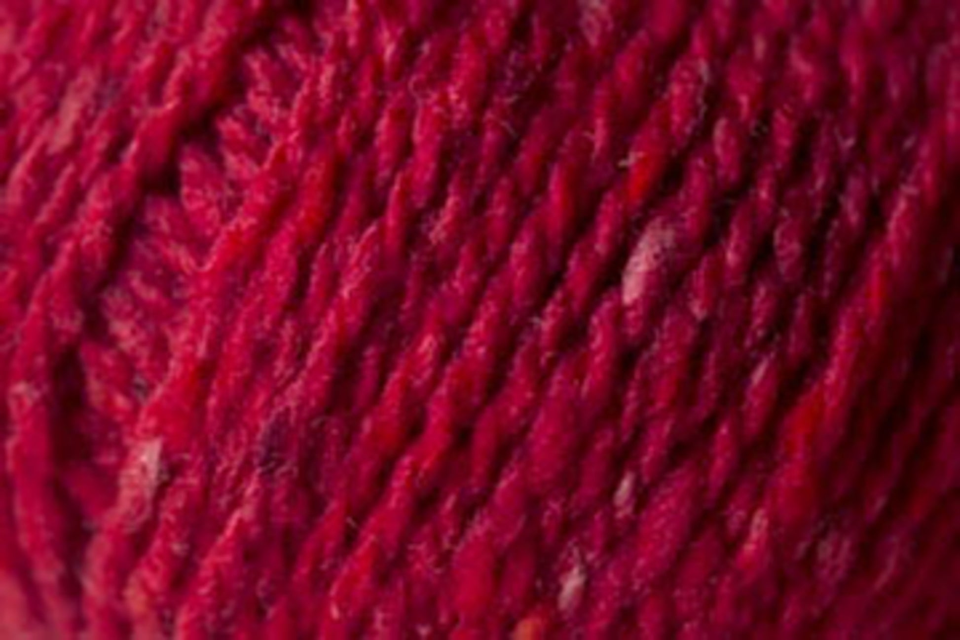 Close-up of a swatch of thick, red yarn. This luxurious fiber, from Kingfisher Yarn & Fibre, showcases the rich red color and subtle variations in shade that create texture and depth. The fibers appear soft and slightly fuzzy, with a tightly twisted structure reminiscent of Jo Sharp Silkroad Aran Tweed.