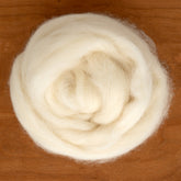 A close-up of a neatly coiled, fluffy ball of Europa Wools Ltd's cream-colored Shetland Top Wool Fiber rests on a wooden surface. The texture appears soft and smooth, ideal for blending into lace knitting projects or spinning fine yarns for intricate crafting.