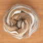 A swirl of Shetland Top Wool Fiber by Europa Wools Ltd, featuring a blend of brown and white hues, is arranged in a circular shape on a wooden surface. The wool's soft and fluffy texture makes it perfect for spinning fine yarns, with the colors blending seamlessly.