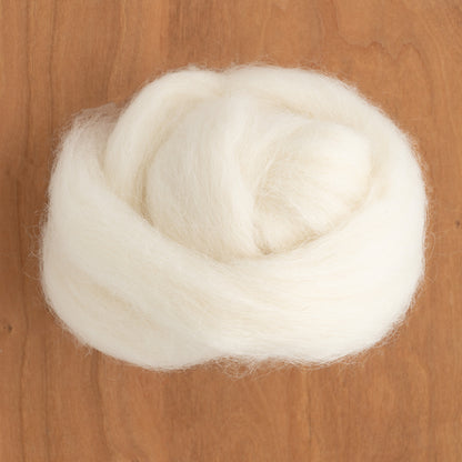 A close-up of a neatly coiled bundle of Icelandic Top Wool Fiber, from Europa Wools Ltd, on a wooden surface, showcasing the unique beauty of the dual-coated fleece from Icelandic sheep.