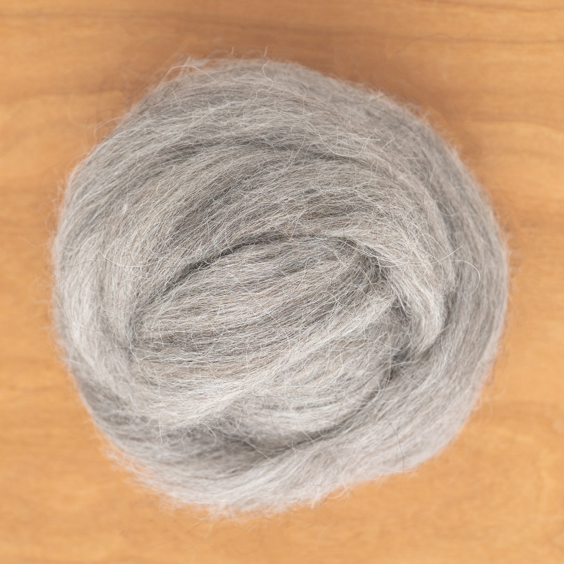 A round, fluffy ball of Icelandic Top Wool Fiber by Europa Wools Ltd, resembling the soft tog fiber from Icelandic sheep, is placed on a wooden surface, showcasing its natural texture.