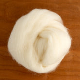 A close-up image of a ball of soft, fluffy white roving wool from Dashing Mouse's Finn Wool Fiber, placed on a wooden surface. The wool is loosely coiled, showing its airy and lightweight texture. The warm brown tone of the wood contrasts with the creamy white color of the lustrous fiber.