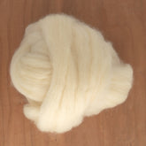 A large bundle of soft Blue Faced Leicester (BFL) Wool Top from Europa Wools Ltd sits on a wooden surface. The cream-colored fibers are fluffy and airy, perfect for spinning into soft yet strong yarns or for felting projects.