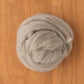 A coiled bundle of soft, grey Blue Faced Leicester (BFL) Wool Top from Europa Wools Ltd rests on a smooth wooden surface. The longwool fiber exhibits a slightly fuzzy texture with strands loosely wrapped in a circular formation.