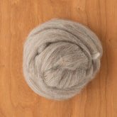 A round bundle of light gray Blue Faced Leicester (BFL) Wool Top by Europa Wools Ltd is neatly coiled on a wooden surface, creating a textured, soft appearance against the smooth background.