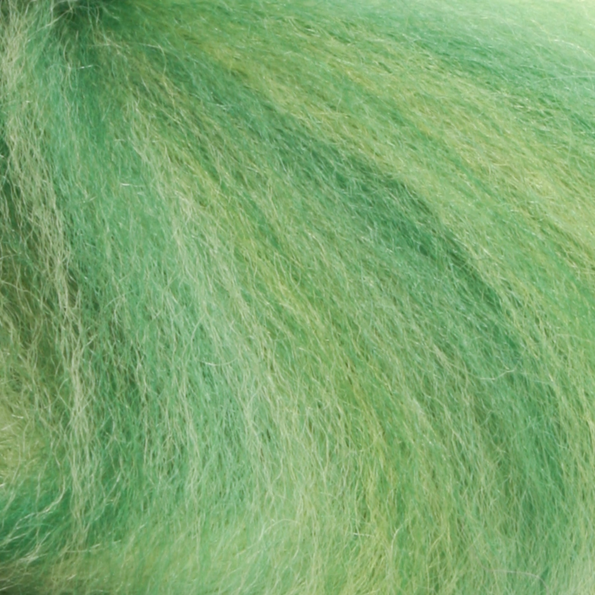 Close-up of the Multi-Colored Merino Wool Top by Europa Wools Ltd, showcasing soft, fluffy fibers in a range of green shades from light to dark. The texture is woolly like merino, with a wavy and slightly tangled appearance.