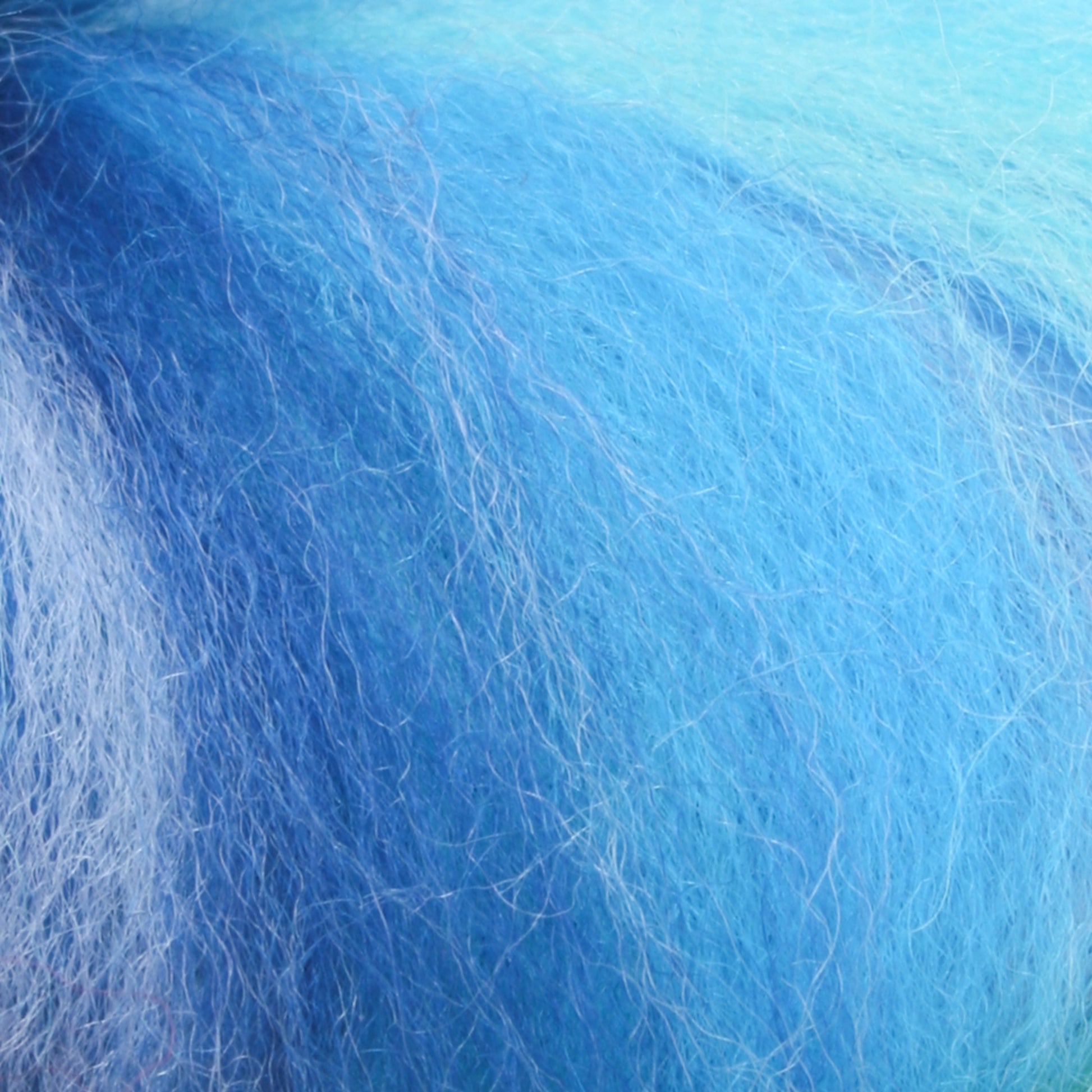 A close-up view of the Multi-Colored Merino Wool Top by Europa Wools Ltd reveals soft, fluffy fibers in varying shades reminiscent of heathered yarns. The texture appears wispy and light, with a blend of vibrant and pastel blues swirling together.