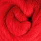 A close-up of vibrant red Corriedale New Zealand wool fibers from Ashford Handicrafts Limited, densely intertwined in a swirl pattern. The texture looks soft and fluffy, making it an ideal choice for spinning fiber enthusiasts.