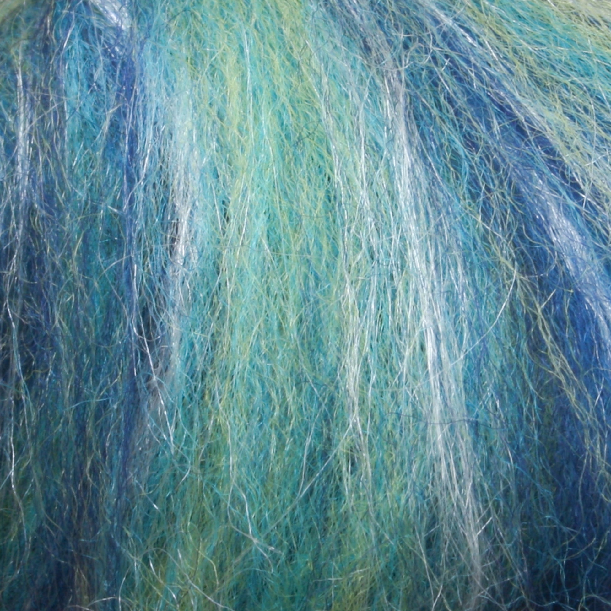 A close-up of the Merino Silk Top Fiber from Europa Wools Ltd reveals its textured fibers in shades of blue, green, and white, intricately interwoven to create a soft and fluffy appearance. Crafted from luxurious yarn, these colors blend harmoniously like abstract brushstrokes on a canvas.