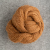 A detailed view of Europa Wools Ltd's Alpaca Top, showcasing its silky soft touch in light brown, neatly coiled against a textured gray background.