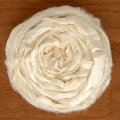 A spiraled arrangement of Dashing Mouse's cream-colored wool roving intertwined with Tussah Silk Top sits on a wooden surface.